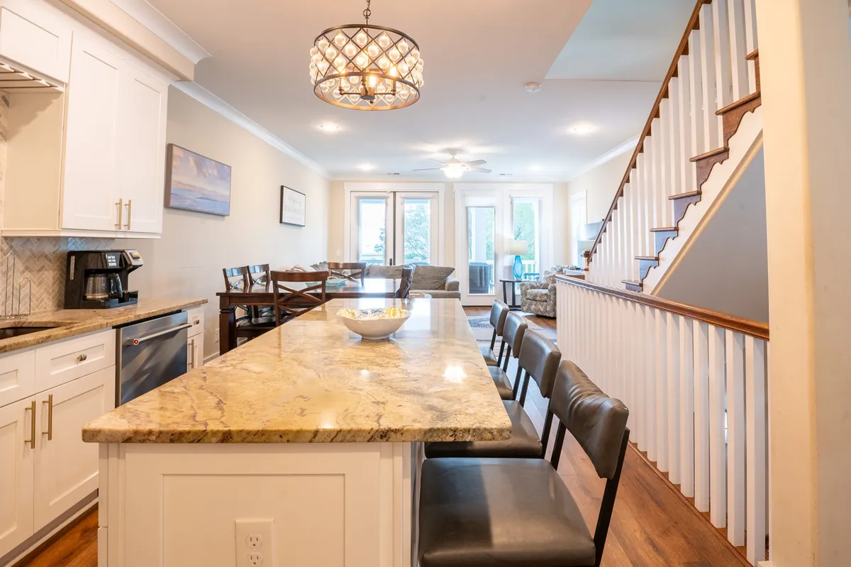 A warmly lit dining area featuring a granite countertop, elegant chandelier, and a wooden staircase. The space feels inviting, perfect for socializing, family gatherings, or entertaining guests between outings, with stylish furnishings that reflect the home's custom design.