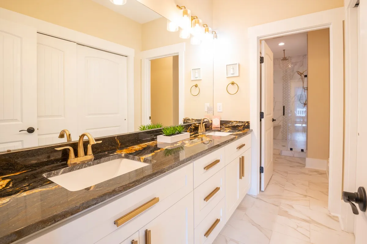 A stylish ensuite bathroom featuring a granite countertop, modern faucet, mirrors with golden accents, and subtle plant decor. The design is serene and luxurious, evoking a spa-like experience for guests.