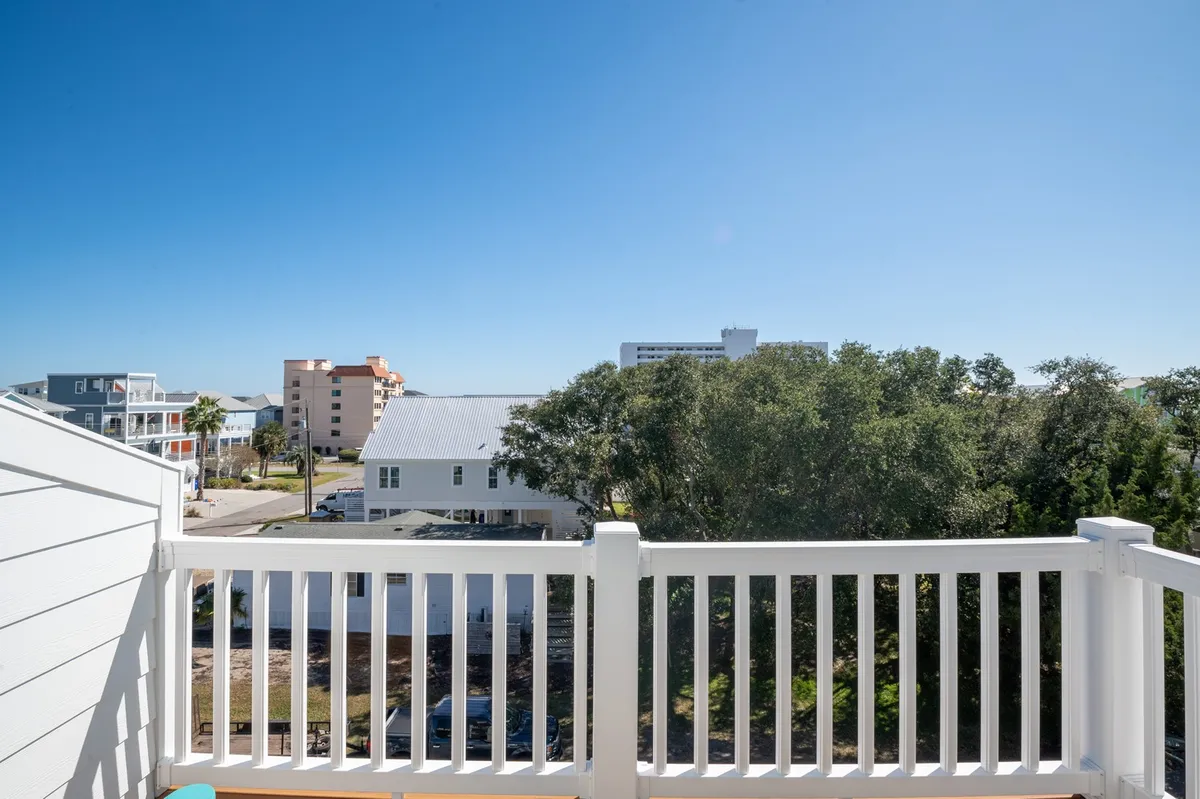 A relaxed balcony perspective with a railing, treetop views, and distant buildings, creating a sense of quiet retreat and outdoor connection. The scene suggests a comfortable space to gather and enjoy the island ambiance after a beach outing.