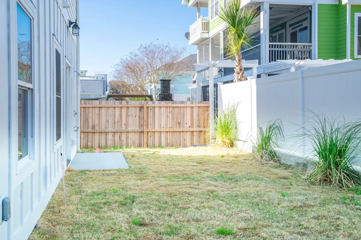 An exterior shot featuring a palm tree, wooden fence, and open yard space. The ambiance is tranquil and the setting is ideal for outdoor gatherings, pet play, or quiet garden moments. Natural elements suggest a connection to the coastal environment.