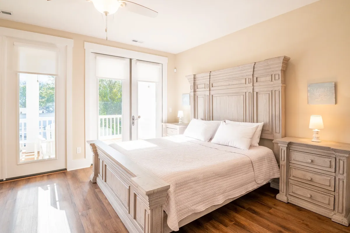 A tranquil bedroom featuring a plush bed, double doors opening to the outside, a nightstand, and a lamp. Sunlight streams into the room, creating a serene and restful atmosphere that suggests a private retreat.