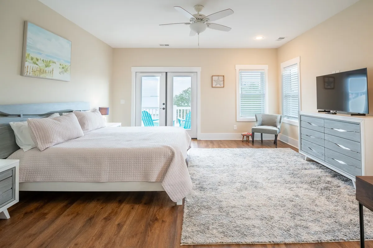 A primary suite with a comfortable bed, balcony doors, armchair, dresser, and television. The room is bright and inviting, with the balcony suggesting access to private outdoor space and beautiful views.