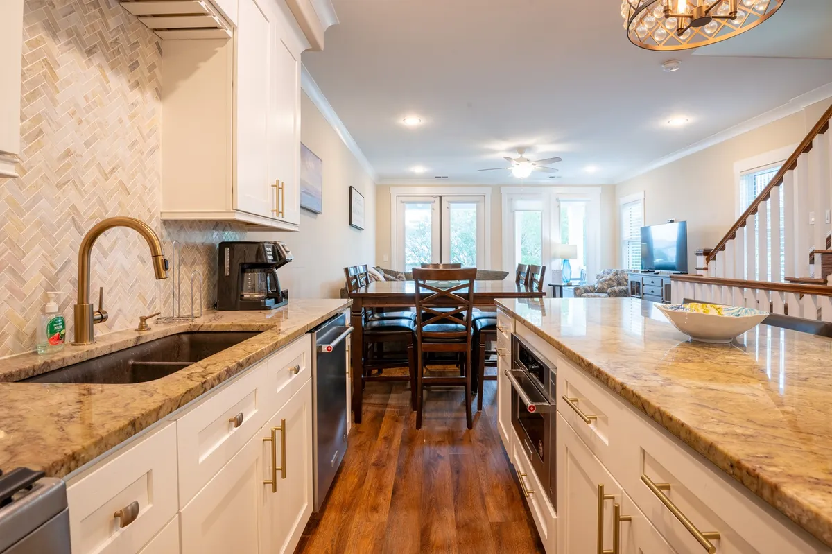 This image showcases the heart of the home's open-concept layout, with a modern kitchen island at the center, an elegant dining area in the background, and a staircase leading upstairs. The space is filled with natural light and offers a clear view of how the kitchen, dining, and living areas seamlessly flow together.