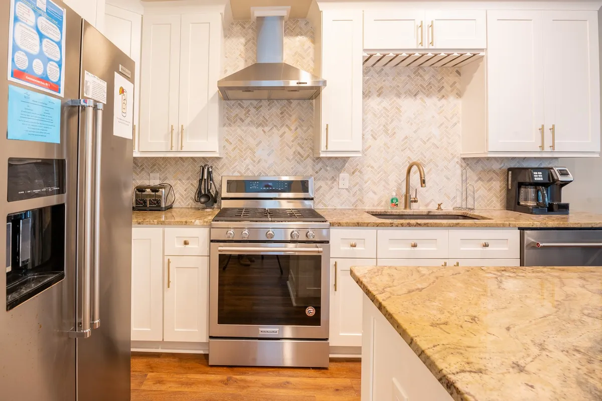 A sleek, modern kitchen with stainless steel appliances, granite countertops, and a herringbone backsplash. The kitchen is set for cooking and entertaining, offering a glimpse of the gourmet amenities described in the section.
