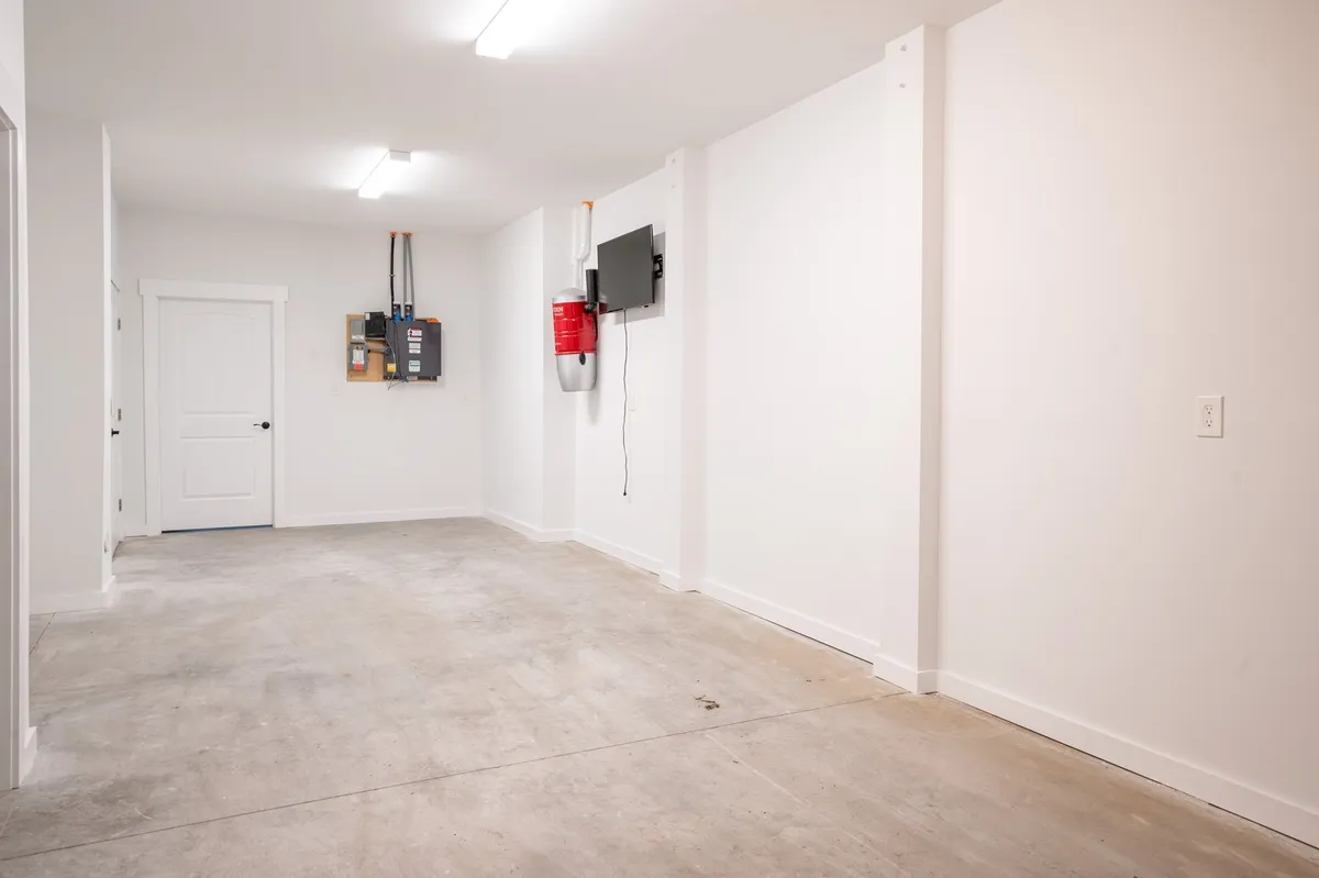 A functional and minimalist garage space featuring a garage door, storage area, and a potential work station. The area is organized and offers plenty of room for parking vehicles or storing tools, reflecting a space where guests can safely and conveniently leave their cars or even pursue DIY projects.