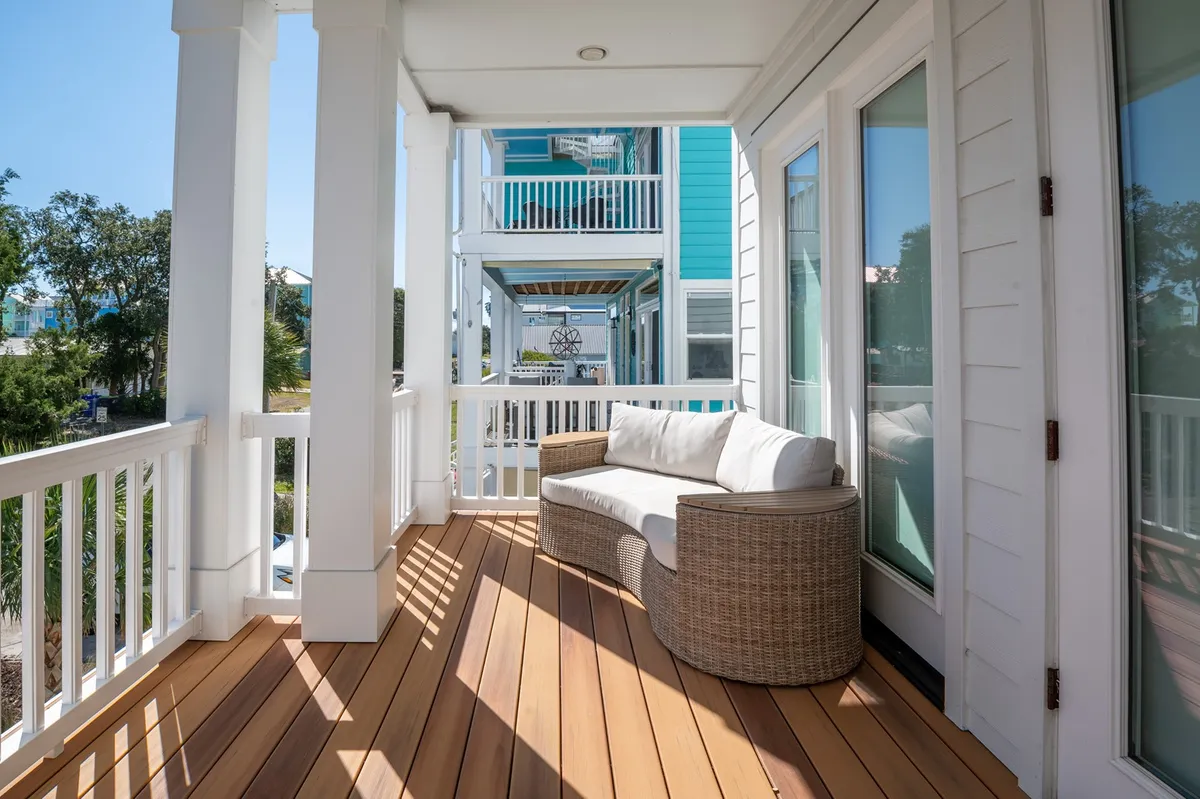 A tranquil, covered porch featuring a wicker couch, wooden flooring, and large windows framed by railings. The atmosphere is peaceful and inviting, with soft natural light enhancing the sense of comfort and seclusion.