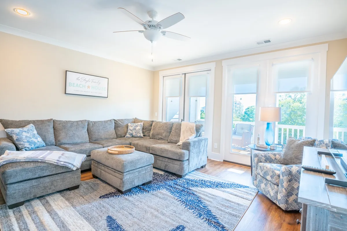 A cozy living area featuring a sectional sofa adorned with decorative pillows, a coffee table, and large windows that flood the space with light. The setup is ideal for relaxing, entertaining, or movie nights, tying in with the idea of family togetherness and comfort.